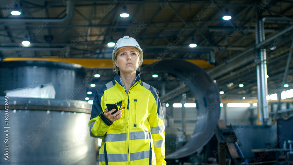 戴着安全帽的女工业工人在重工业马努穿行时使用手机