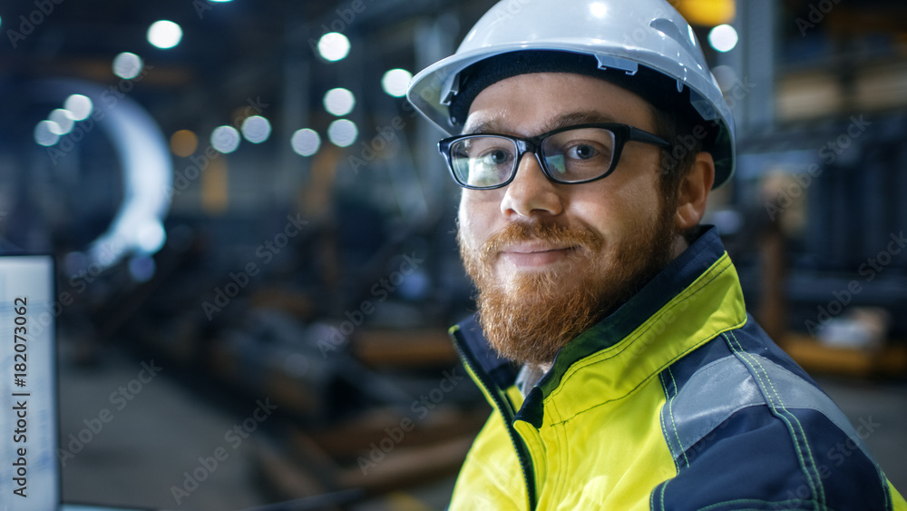  Industrial Engineer Wearing Hard Hat,  Safety Jacket and Glasses Smiles on Camera. He Works in Big 