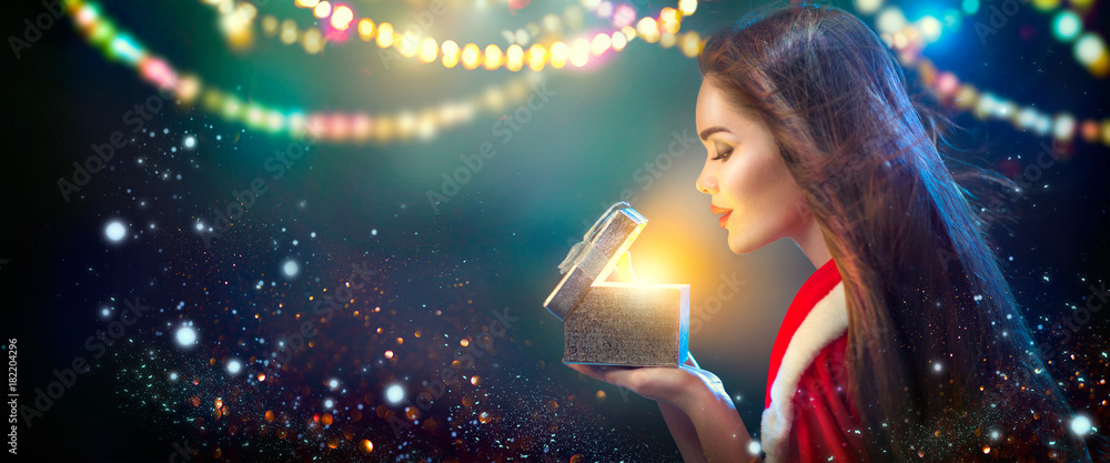 Christmas scene. Beauty brunette young woman in party costume opening gift box over holiday blurred 