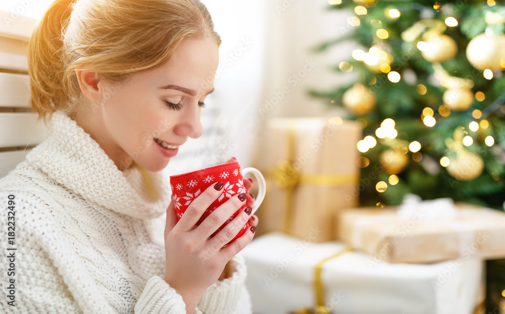 在圣诞树旁拿着一杯茶的快乐女人。