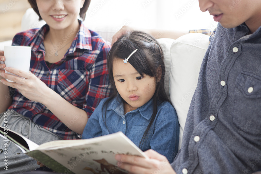 Dad and mommy are reading picture books for their daughter.