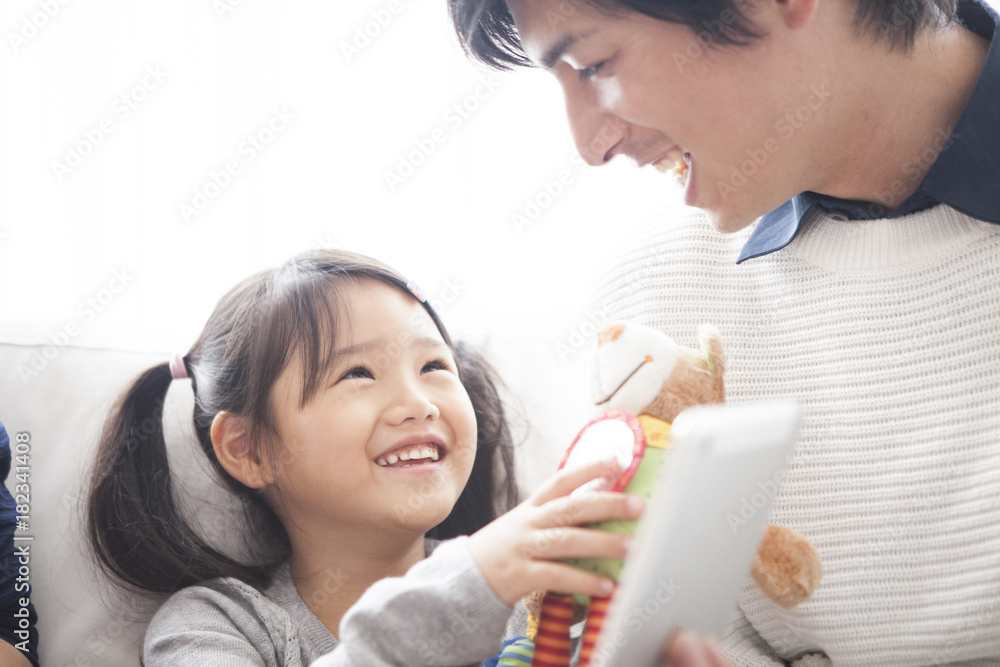 父母和女儿坐在沙发上，一起使用数字平板电脑。