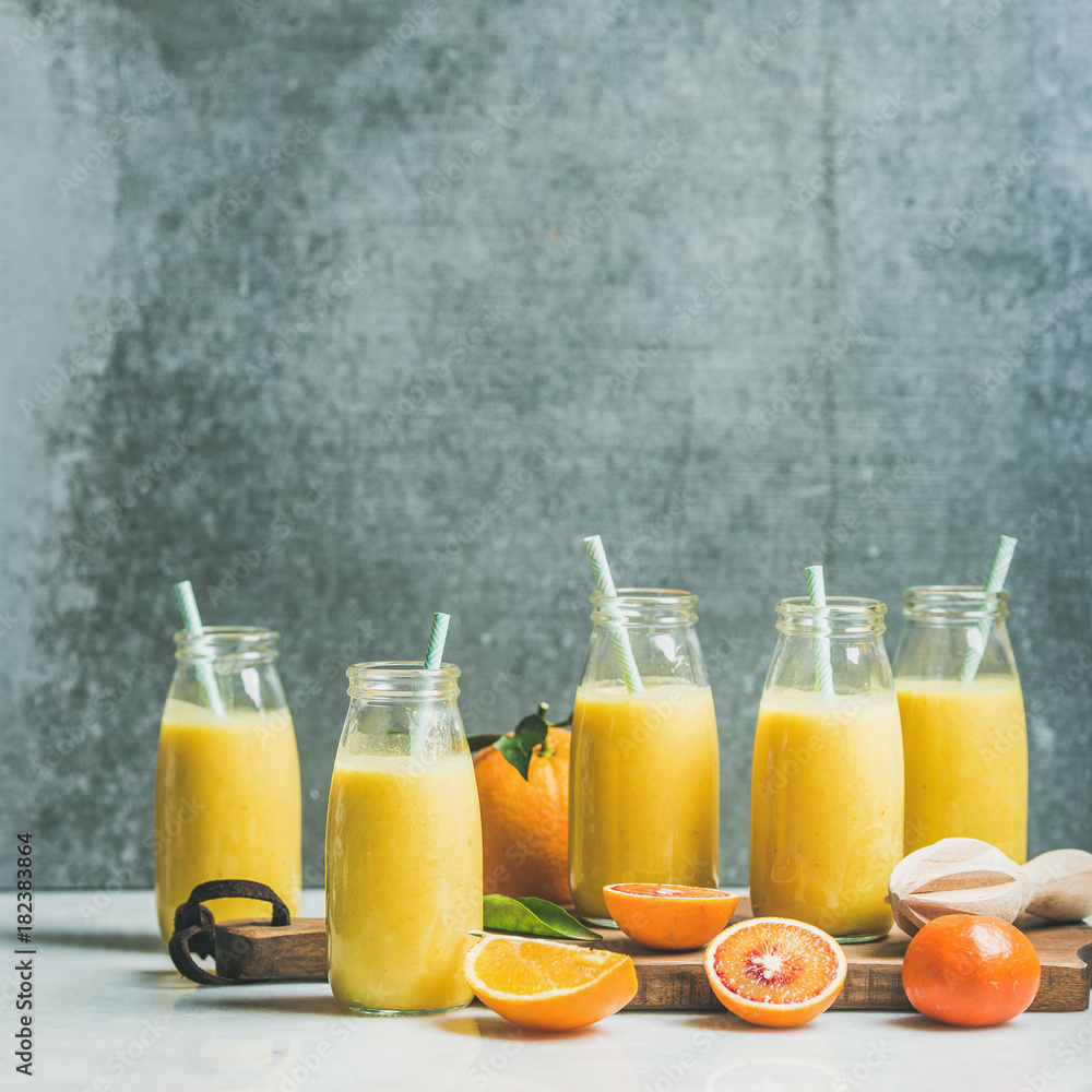健康的黄色奶昔，装在浅色大理石塔上的木板上，装着柑橘类水果和生姜