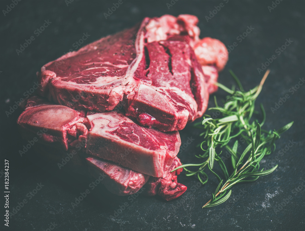 新鲜生的未煮熟的牛肉t骨牛排的特写，与迷迭香放在黑斯顿上