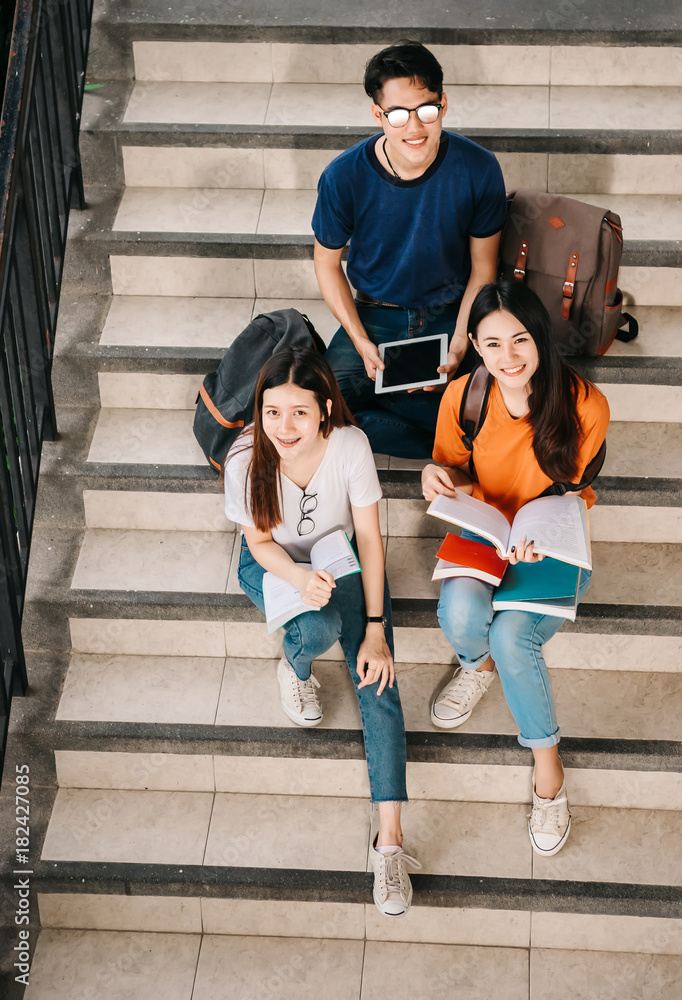 一群年轻或十几岁的亚洲学生在大学里微笑着读着书，看着ta