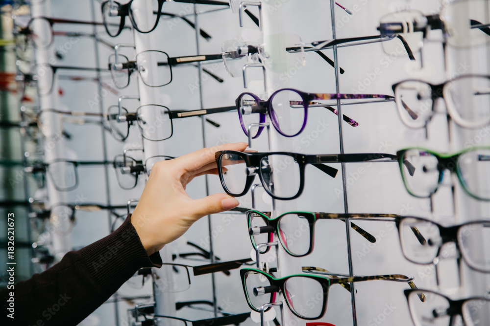 带着眼镜站在眼镜店里。女人的手会选择眼镜。