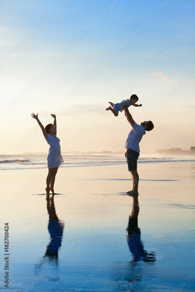 父亲在空中高高抛婴儿儿子，母亲在水池旁跳跃。快乐的一家人在阳光下漫步