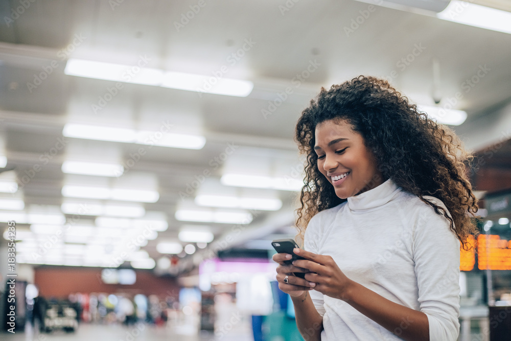 机场里的年轻女子，手里拿着智能手机发短信。