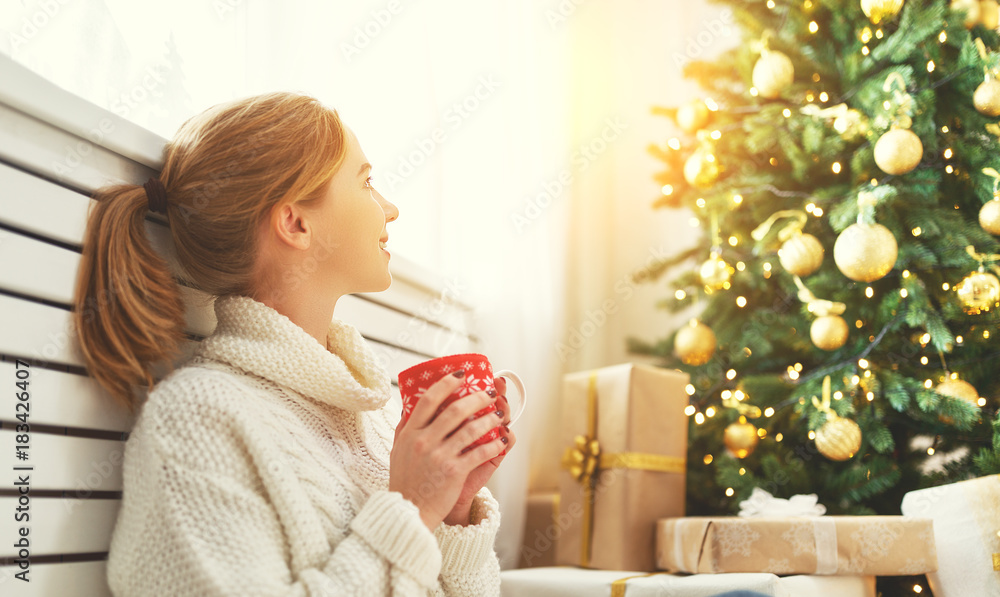在圣诞树旁拿着一杯茶的快乐女人