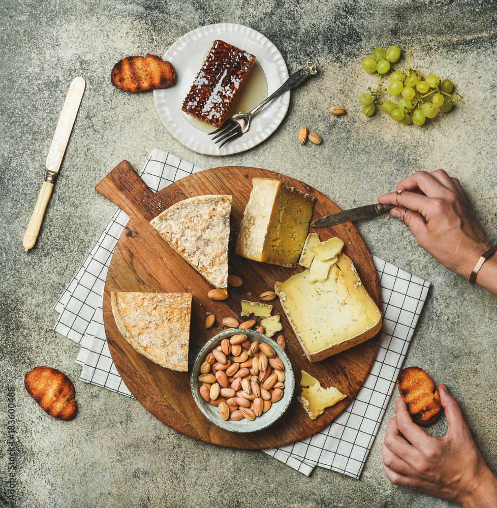 扁平的奶酪拼盘，配各种奶酪、绿葡萄、蜂蜜和坚果，配女性手
