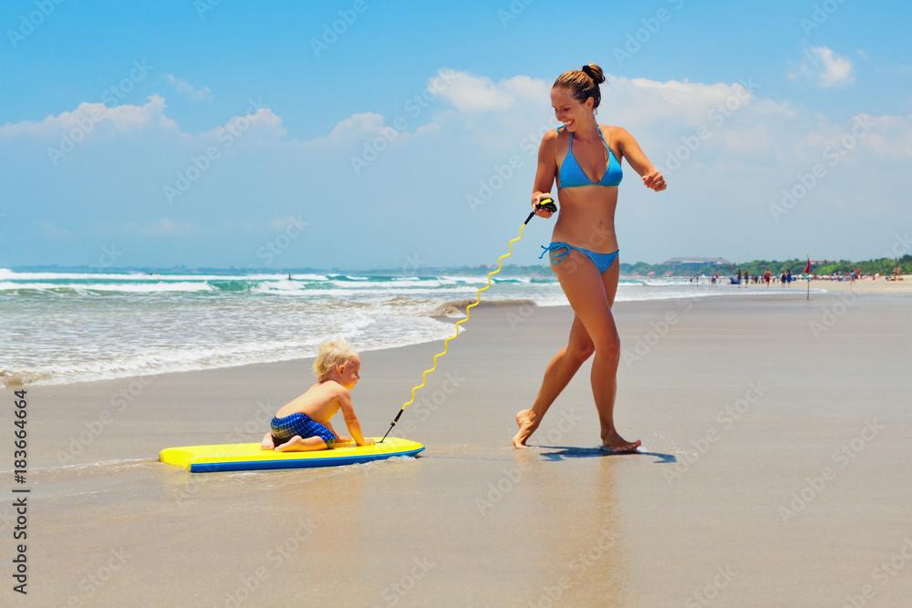 快乐的一家人玩得很开心——妈妈在海浪边的水池边跑步，把小儿子拉上冲浪板