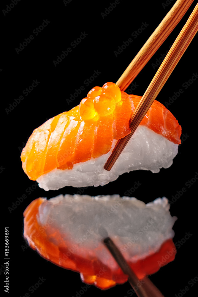 筷子里的三文鱼寿司nigiri被隔离在黑色背景上，有反光。特写。