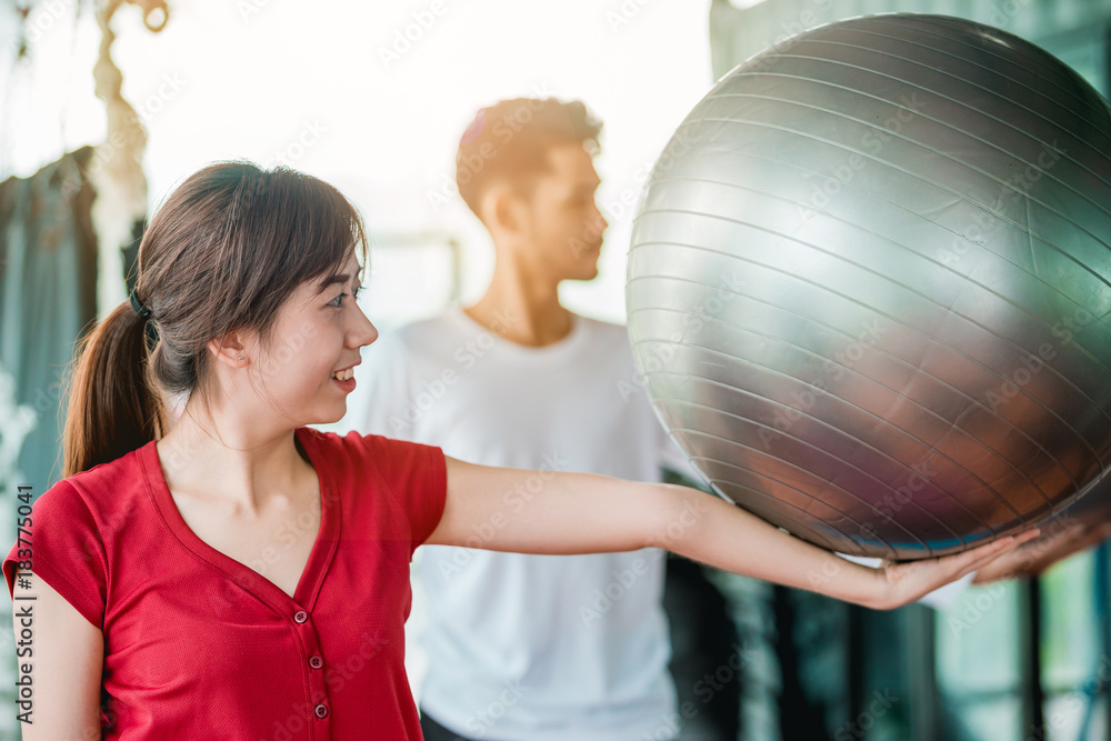 Asian girl and man exercises with a fitness ball in the fitness center with happiness.