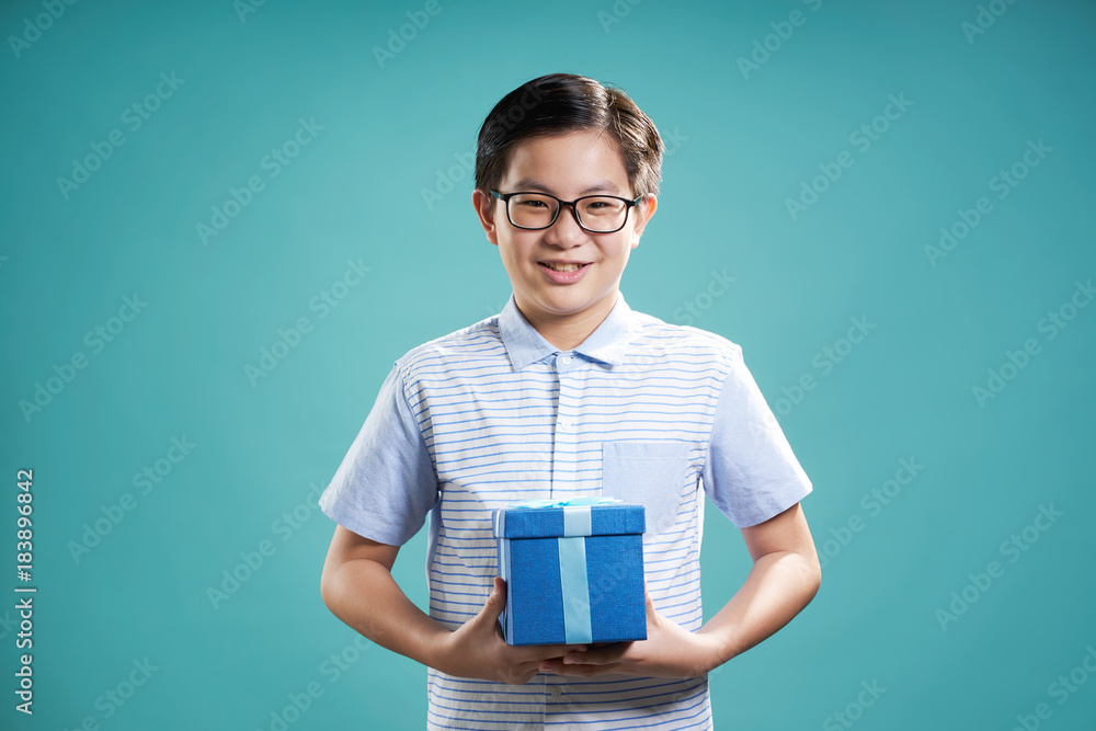 亚洲快乐小男孩的特写肖像，粉色礼物盒，隔离在浅蓝色背景上