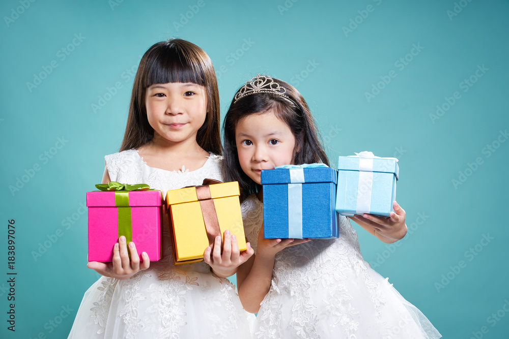 两个亚洲小女孩拿着生日礼物的肖像，孤立在浅蓝色背景上。