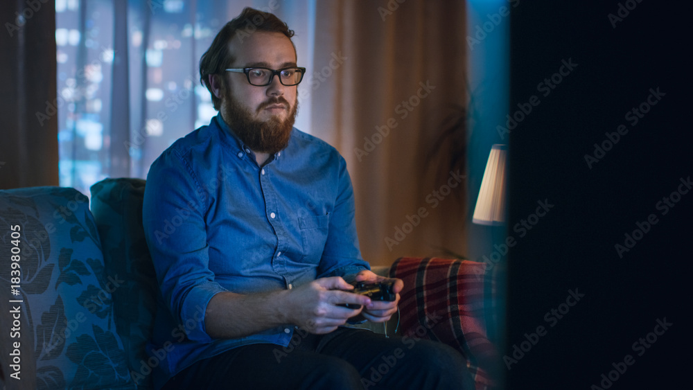 晚上男人坐在沙发上，在客厅玩电子游戏。大城市就在眼前