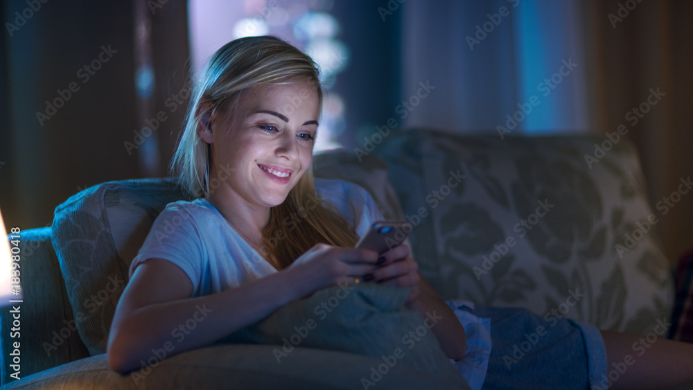 深夜美女躺在客厅的沙发上，用智能手机微笑