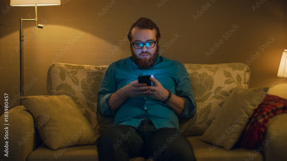 一名男子坐在客厅沙发上，使用智能手机拍摄的肖像。落地灯亮了
