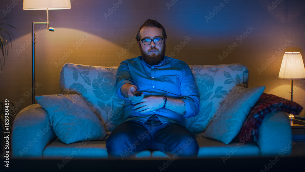 一名男子坐在客厅沙发上看电视、换频道的人像照片。L层
