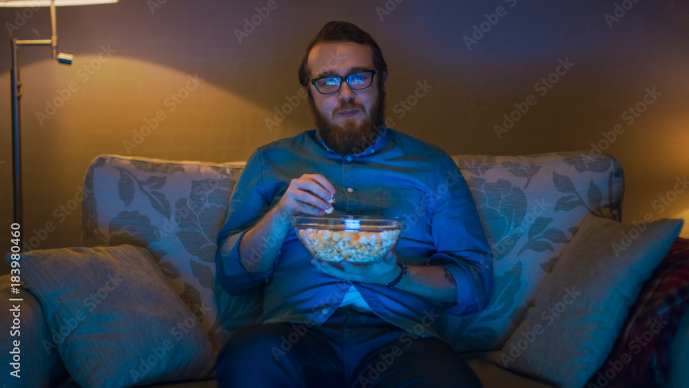 一个男人坐在客厅沙发上吃爆米花看电视的肖像照片。L层