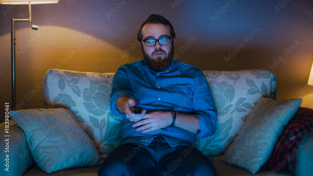 一名男子坐在客厅沙发上吃爆米花看电视的肖像照片。L层
