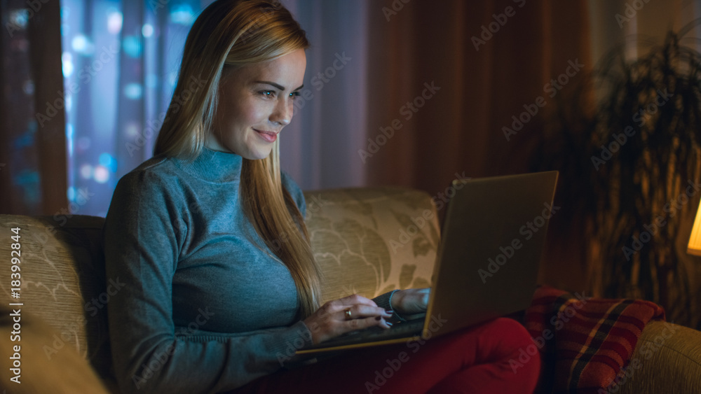 漂亮的年轻女人在客厅用笔记本电脑工作，她坐在沙发上用笔记本o