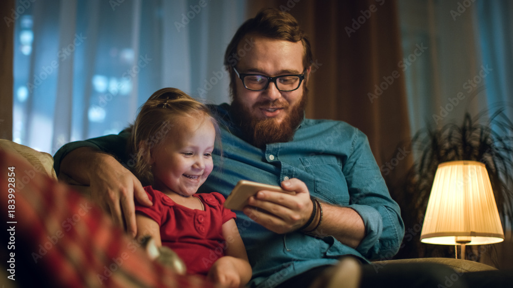 晚上父亲和小女儿坐在客厅的沙发上看有趣的视频