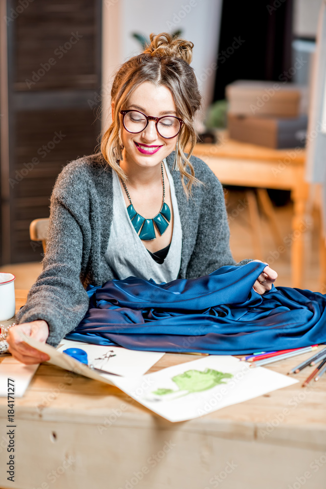年轻的女时装设计师，穿着蓝色面料，坐在美丽的办公室里，与众不同