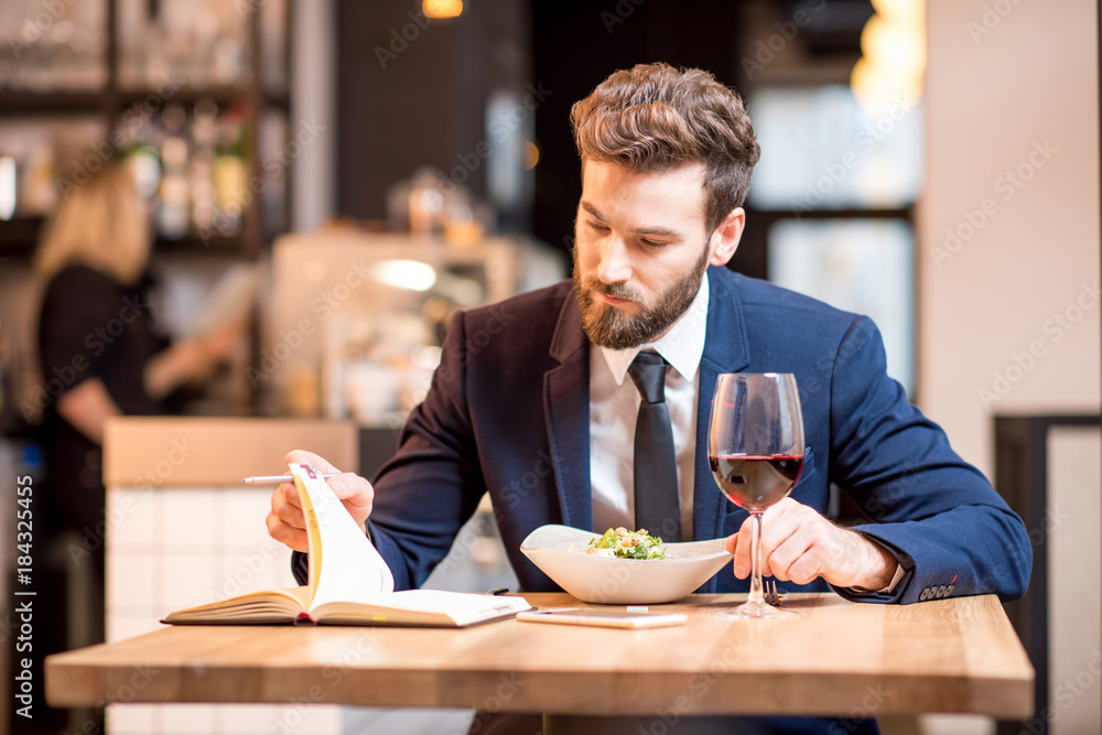 穿着西装的优雅商人坐在现代餐厅享用沙拉和葡萄酒