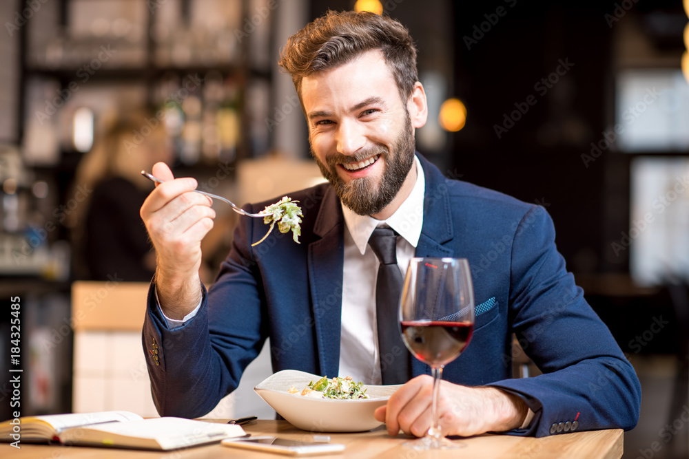 穿着西装的优雅商人坐在现代餐厅享用沙拉和葡萄酒