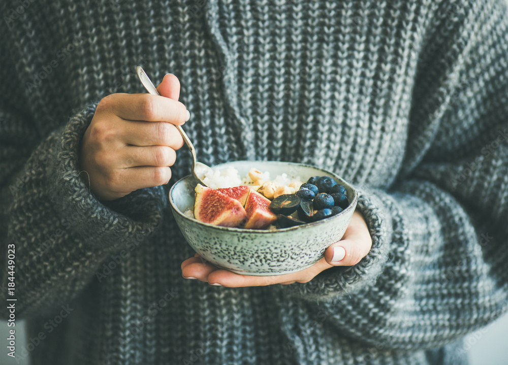 健康的冬季早餐。穿着灰色羊毛衫的女人在吃无花果椰子粥，berri