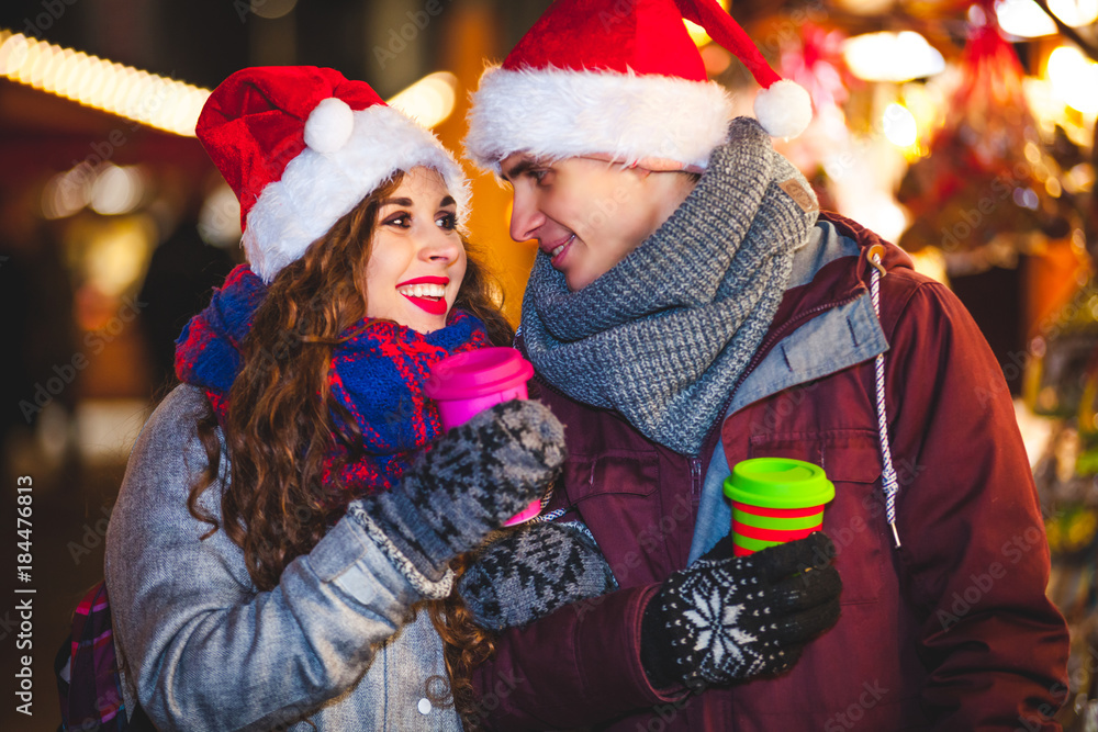 一对幸福的情侣，穿着暖和的衣服，喝着热饮，晚上享受圣诞集市
