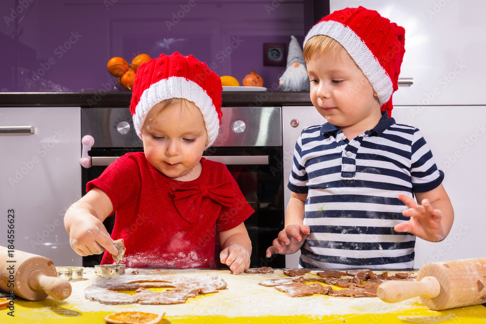 Cute little boy and girl twins preparing Christmas cookies in the kitchen