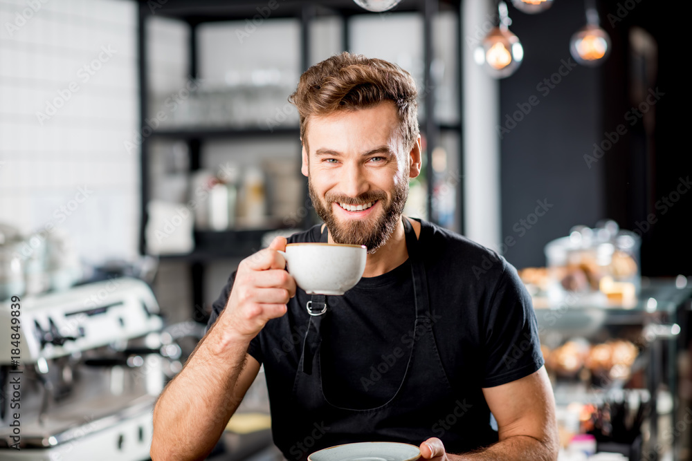 Portrait of a handsome barista sitting with coffee at the bar of the modern cafe interior