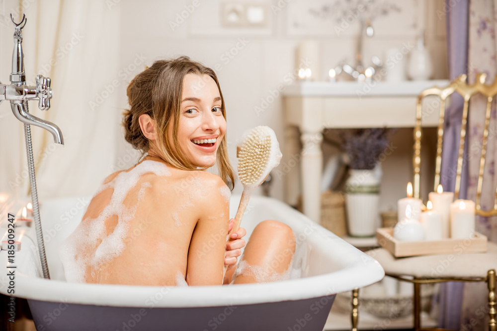 年轻顽皮的女人在浴室里充满泡沫的漂亮复古浴缸里用刷子清洗