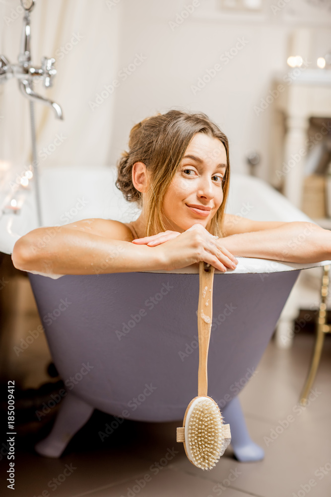 一位美女的画像，她拿着刷子躺在复古浴室的复古浴缸里