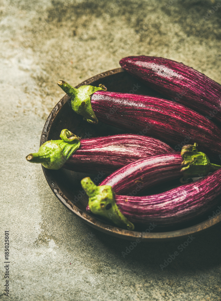 Fresh raw Fall harvest purple eggplants or aubergines in wooden bowl over grey concrete stone backgr