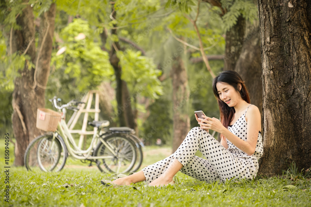 亚洲女性在公园户外的生活方式，使用智能手机在夏天放松快乐