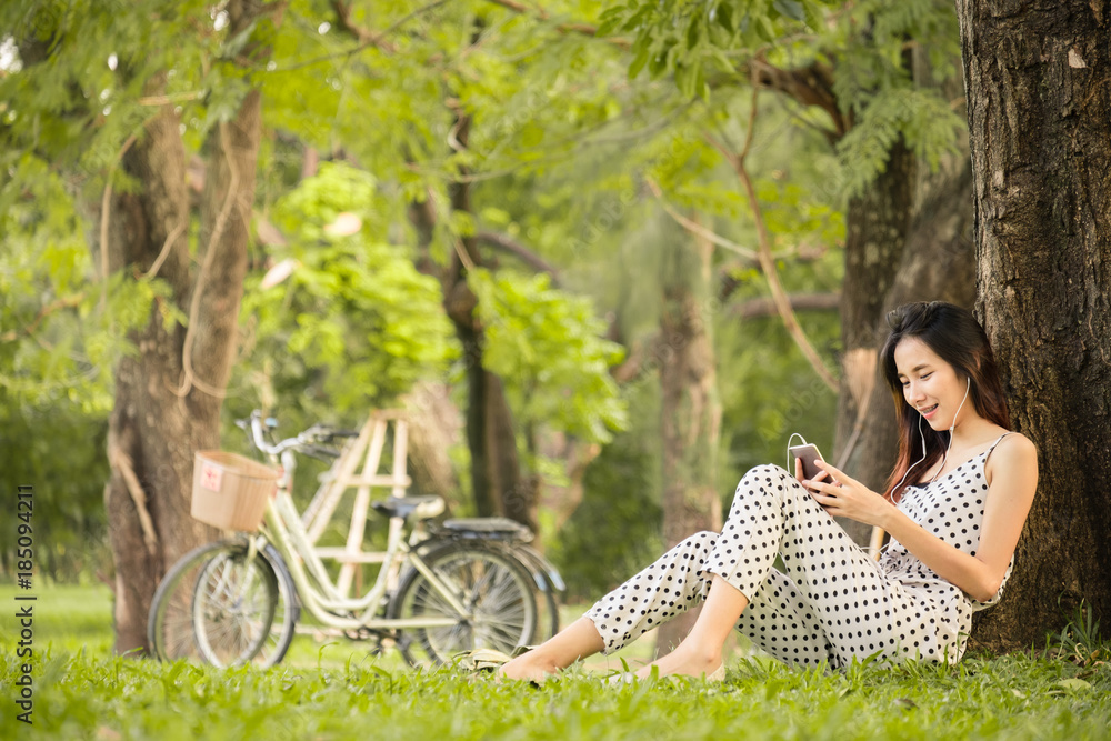 亚洲女性在公园户外的生活方式，使用智能手机听音乐放松和快乐