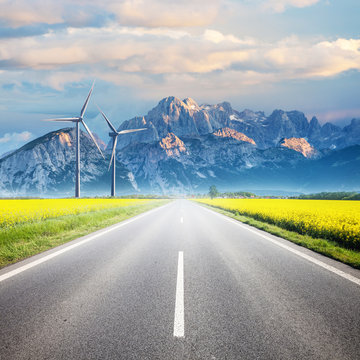 夏季田野和山区之间的柏油路，风力发电涡轮机在地平线上