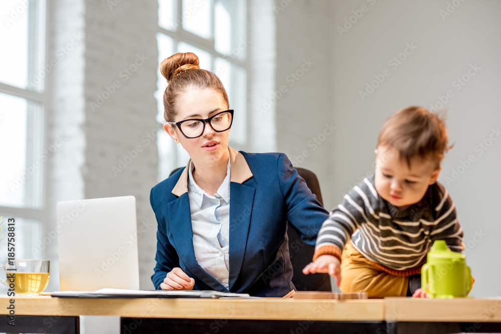 年轻的多任务女商人穿着西装，和他坐在一起处理笔记本电脑和文件