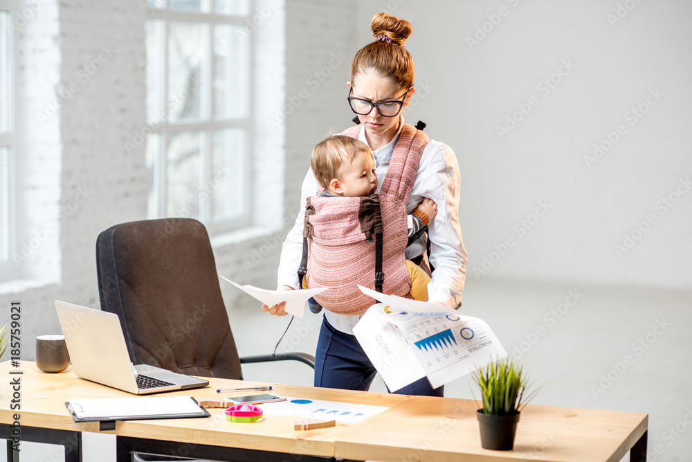 Exhausted businesswoman working with paper documents with her baby son at the office