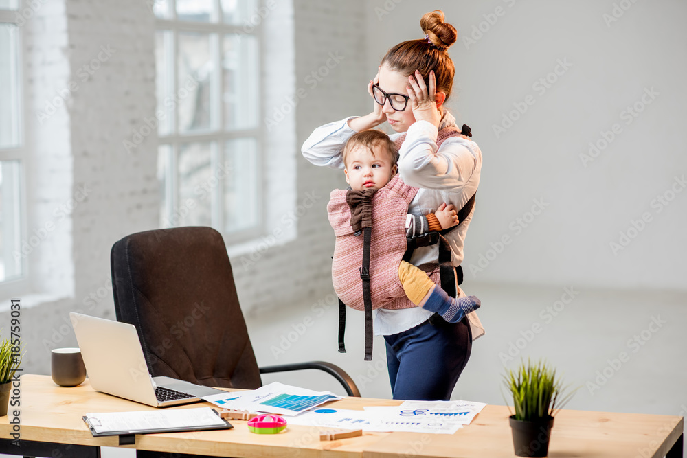 疲惫的女商人在办公室抱着她的小儿子站着头工作