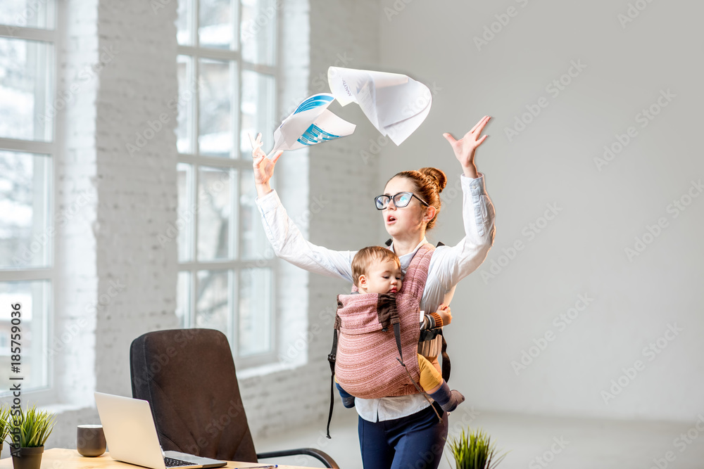 Multitasking and exhausted businesswoman throwing up a documents standing with her baby son during t