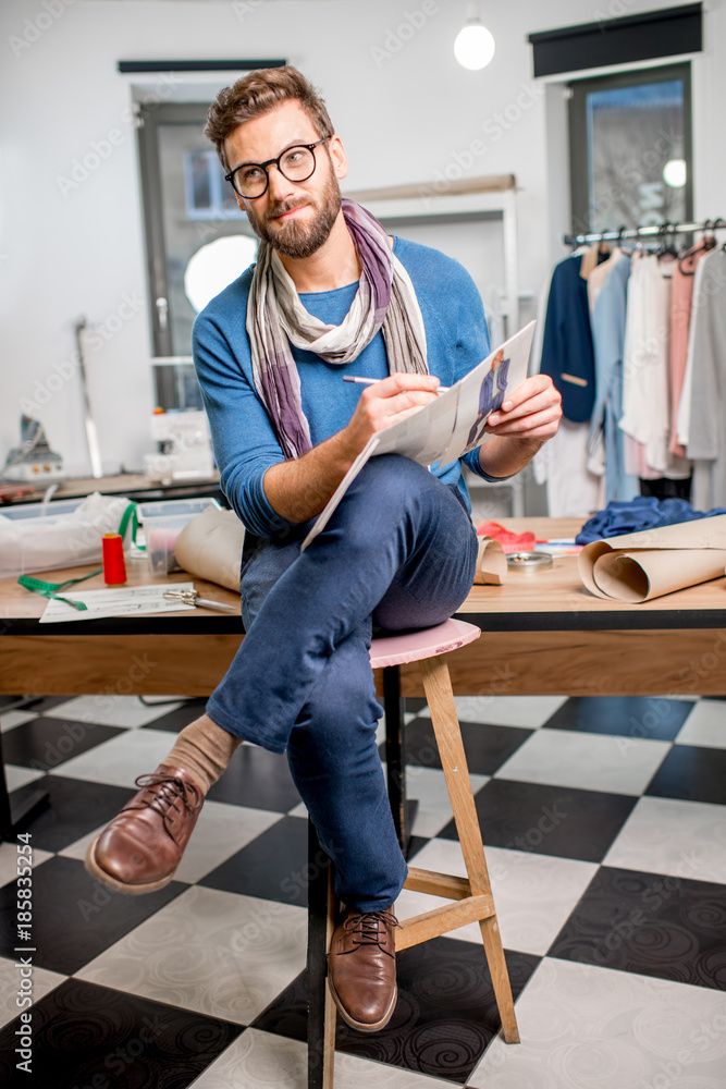 一位英俊的时装设计师的肖像，与服装草图坐在满是泰洛里人的工作室里