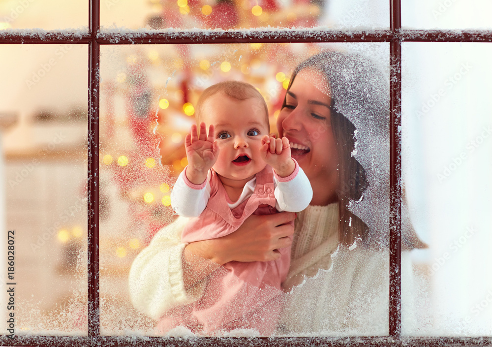 母亲手中的可爱女婴透过窗户看，家庭寒假