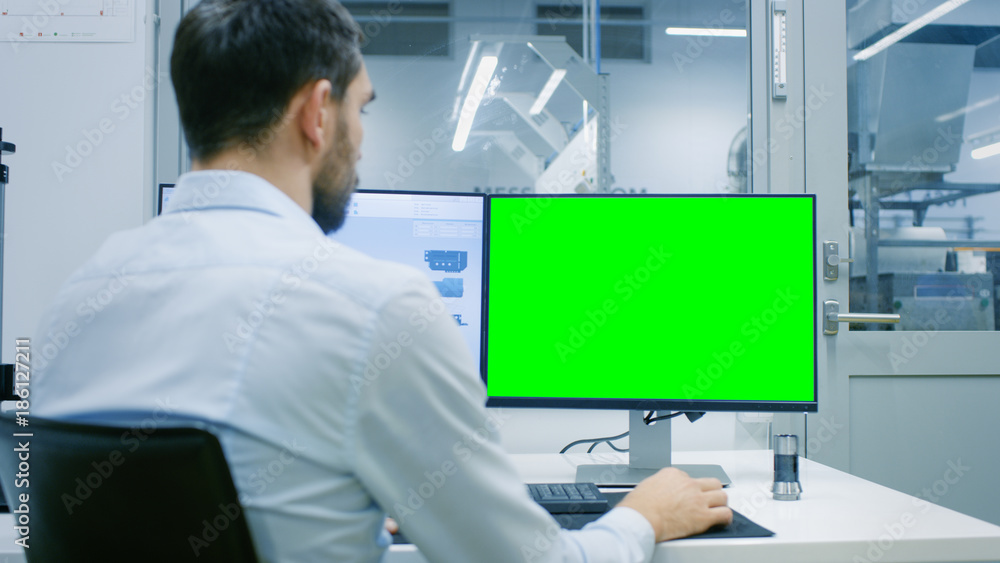 工程师/技术员在有两个显示器的个人电脑上工作，一个有绿屏Chroma