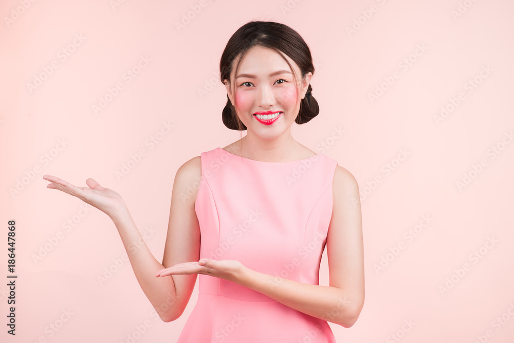 可爱的亚洲年轻女性，带着时尚的妆容，手在粉色上展示出孤立的东西。