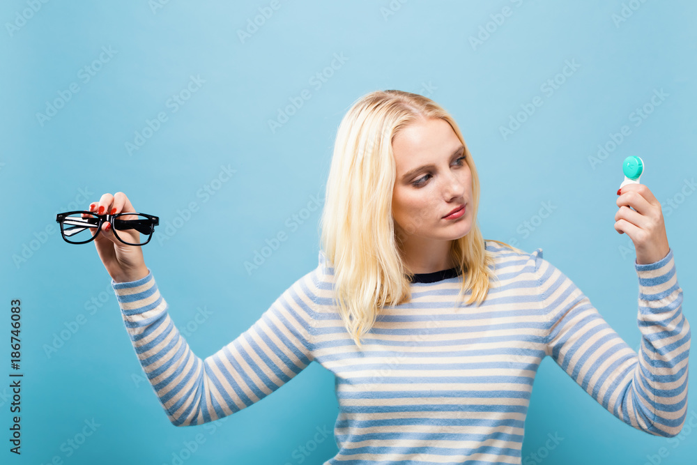 年轻女性在固体背景下选择隐形眼镜或眼镜