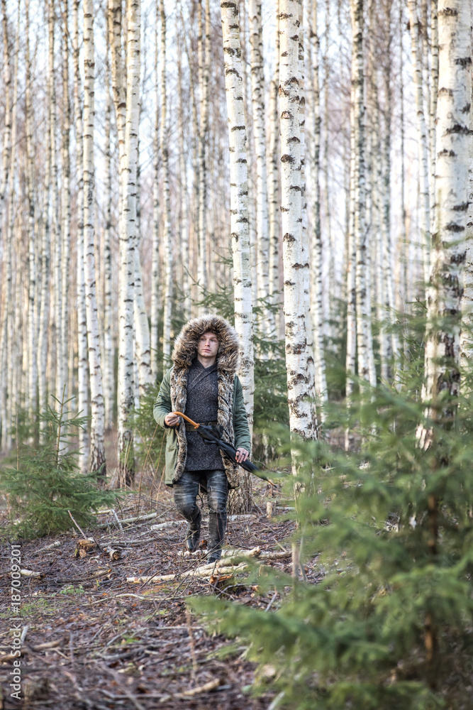 一个年轻人在森林里穿着绿色的冬季派克大衣，提着行李箱。